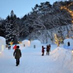 Yunishigawa Onsen Kamakura Festival at dusk, featuring glowing snow huts, winter lights, and visitors exploring the snowy village.