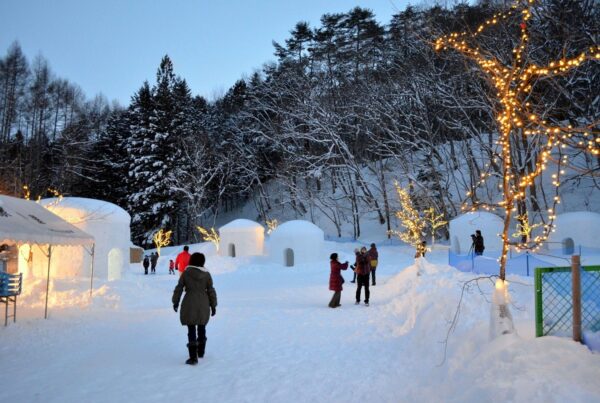 Yunishigawa Onsen Kamakura Festival at dusk, featuring glowing snow huts, winter lights, and visitors exploring the snowy village.