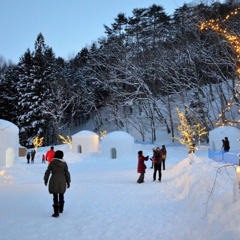 Yunishigawa Onsen Kamakura Festival at dusk, featuring glowing snow huts, winter lights, and visitors exploring the snowy village.
